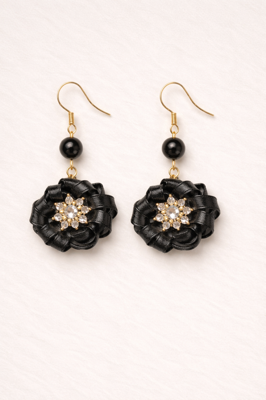 Black flower-shaped earrings with gold accents on a white background