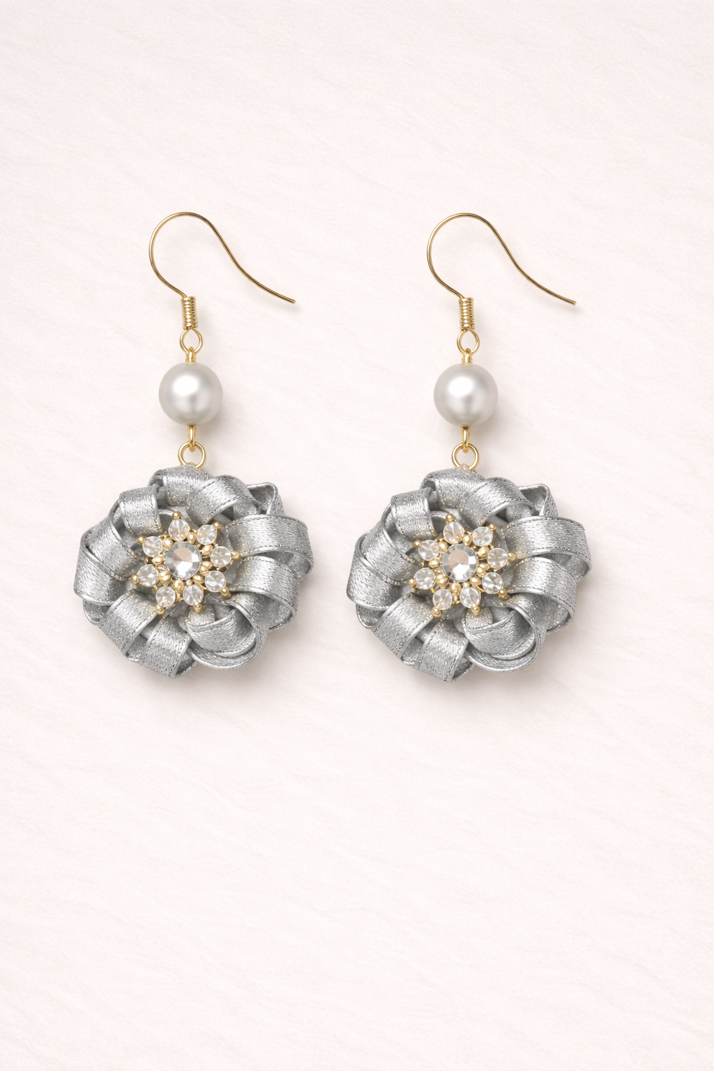 Pair of silver floral earrings with pearl accents on a light pink background